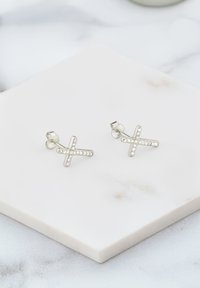 Silberne Kreuzohrringe mit klaren Strasssteinen, die ein poliertes Finish und ein einfaches Design aufweisen, präsentiert auf einer glatten Marmoroberfläche.