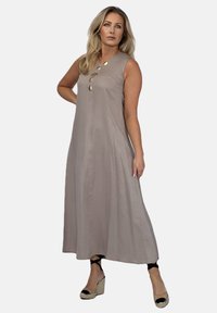 Bez rękawów, długa beżowa sukienka o luźnym kroju. Posiada okrągły dekolt i ozdobne złote guziki wzdłuż przodu. Gładka tekstura materiału.