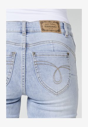 Světle modré džíny z denimu s tmavým prošíváním. Obsahují dvě zadní kapsy s dekorativním šitím a hnědou koženou visačkou na pase.