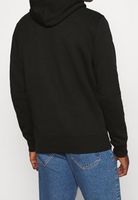 Sudadera negra con capucha ajustable, puños y dobladillo acanalados, combinada con unos jeans de mezclilla de color azul claro con detalles de costura.