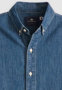 Camicia in denim blu con colletto button-down, caratterizzata da bottoni bianchi e una texture sottile. L'etichetta indica il marchio Levi Strauss & Co., taglia M.