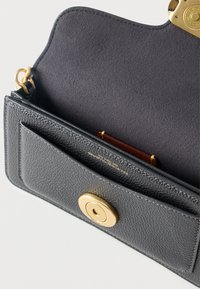 Μαύρη τσάντα χεριού από δέρμα με υφή χαλικιών, με ανοιχτό καπάκι που αποκαλύπτει λείο εσωτερικό φόδρα και χρυσό κυκλικό μαγνητικό κούμπωμα.