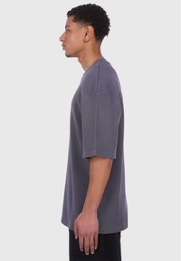 T-shirt gris à manches courtes en tissu texturé, coupe décontractée, avec un col rond et un détail côtelé aux manches.
