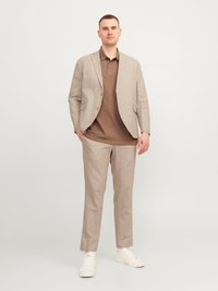 Beige lněný blazer přes hnědé polo triko, spárovaný s světle béžovými kalhotami a bílými teniskami. Minimalistický design s přiléhavým střihem.