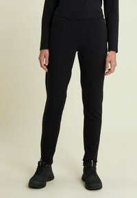 Pantalones joggers ajustados negros hechos de tela suave con una cintura elástica y sin patrones visibles. Usados con zapatos deportivos negros.