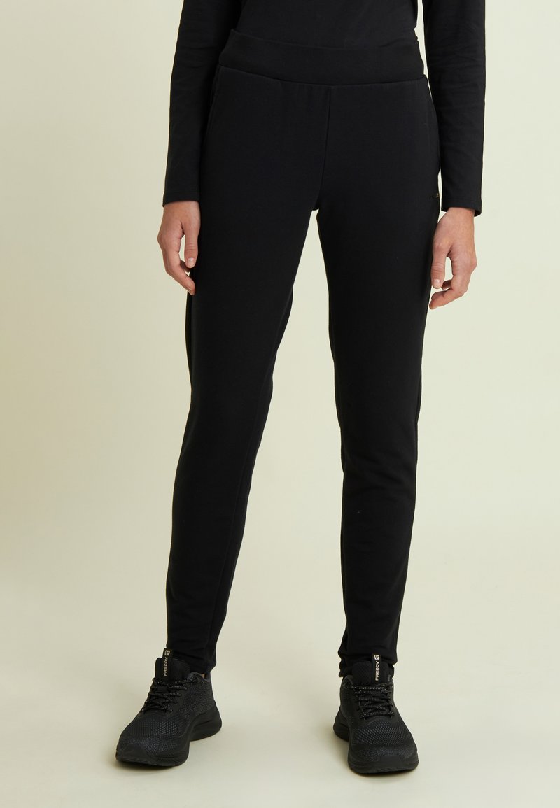 Pantalones joggers ajustados negros hechos de tela suave con una cintura elástica y sin patrones visibles. Usados con zapatos deportivos negros.