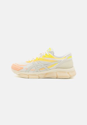 Kevyt juoksukenkä, jossa on hengittävä verkkomateriaali, keltaisia ja oransseja yksityiskohtia, pehmustettu beige välipohja ja kumipohja.