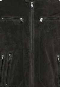 Zwarte suède jas met meerdere ritszakken, een gladde textuur en zilverkleurige hardware. Beschikt over een staande kraag en strakke lijnen.