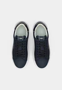 Tenisice u mornarsko plavoj boji s glatkim gornjim dijelom, bijelim potplatima i crnim vezicama. Na jeziku i bočno je vidljiv detalj logotipa. Minimalistički dizajn.