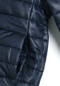 Doudoune bleu marine avec texture matelassée, dotée de coutures horizontales et d'une finition lisse et brillante. Conception légère et compacte.