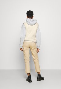 Beżowe spodnie cargo i szara polarowa bluza z kapturem, widok z tyłu, charakteryzujące się luźnym krojem i minimalnymi detalami. Czarne buty wojskowe.