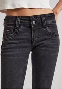 Svarta denimjeans med en figurnära design, som har dubbelknäppning och femficksstil. Tyget har en lätt textur.