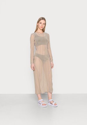 Vestido beige transparente com mangas longas, apresentando riscas verticais roxas. Combinado com sandálias roxas claras sobre um fundo simples.