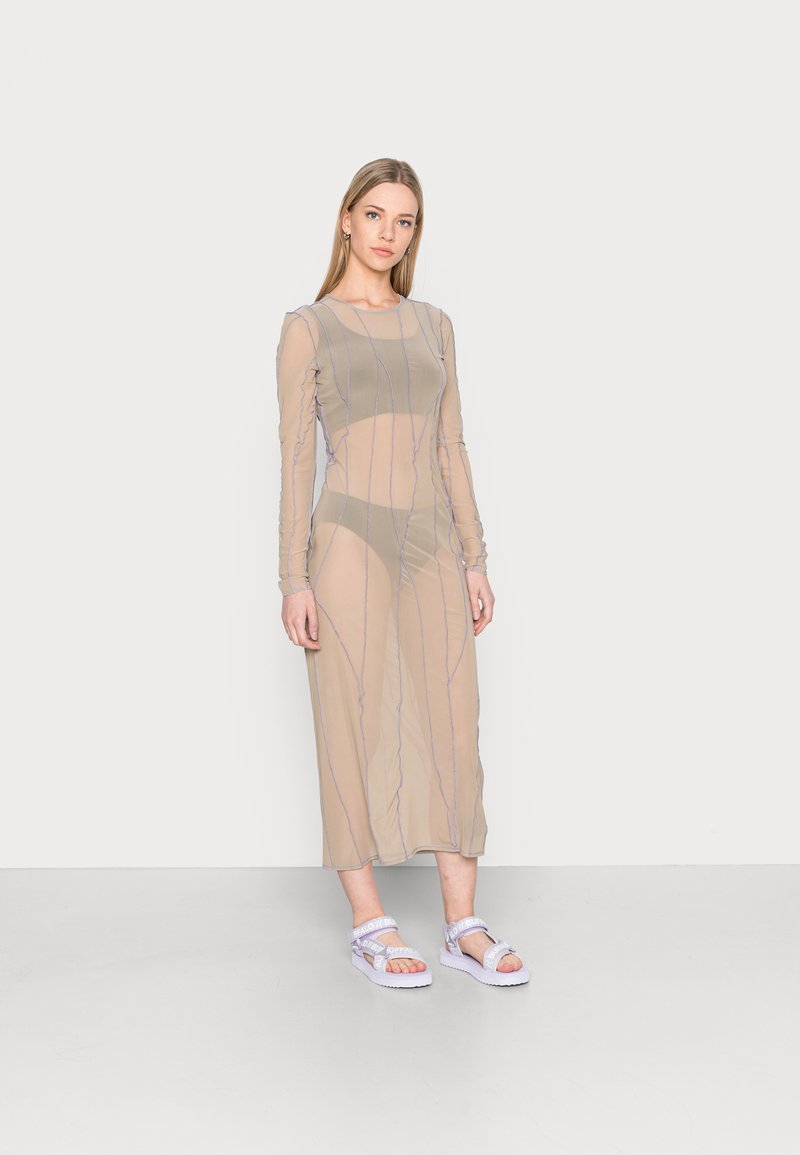 Vestido beige transparente com mangas longas, apresentando riscas verticais roxas. Combinado com sandálias roxas claras sobre um fundo simples.