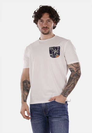 Camiseta blanca de manga corta hecha de algodón, con un bolsillo azul con un patrón de palmeras, combinada con jeans de mezclilla azules.