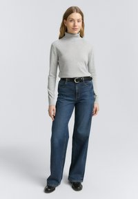Ljust grå turtlenecktröja, kombinerad med högmidjade, vida mörkblå jeans, fästa med ett svart bälte. Slät textur, enkel design.