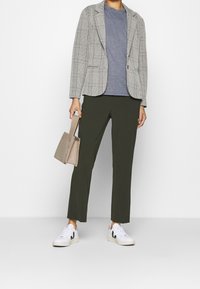 Blazer a cuadros en gris y blanco, camiseta azul, pantalones verde oliva, bolso texturizado beige, zapatillas blancas con acentos negros.