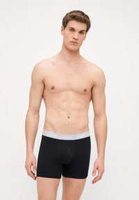 Čierne boxerské trenky so soft šedým pásom s logom "HUGO". Úzky strih s minimálnymi švami pre pohodlie. Model je bez trička.