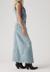 Hellblaues Denim-Westen kombiniert mit einem langen, fließenden Denim-Rock. Der Rock hat einen ausgefransten Saum und wird mit schwarzen Absatzstiefeln getragen.