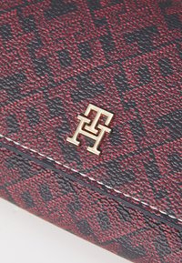 Red and navy textured material handbag featuring a gold logo accent and white stitching along the edges. Distinctive geometric pattern throughout.