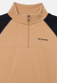 Pull en polaire beige avec un col montant, manches raglan noires, fermeture éclair et logo Columbia brodé sur la poitrine. Texture douce.