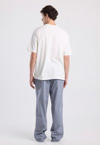 Witte katoenen t-shirt met korte mouwen, gecombineerd met blauw-witte gestreepte broek, met een ontspannen pasvorm en rechte snit.