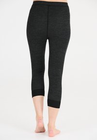 Svarta capri leggings gjorda av texturerad tyg, med en åtsittande design och kontrasterande svarta vristhällor. Släta sömmar löper vertikalt.