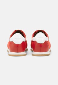 Sneakers in rete rosso e pelle con accenti bianchi, forma arrotondata e suola in gomma. Presentano linguette sul retro per un facile indossamento.