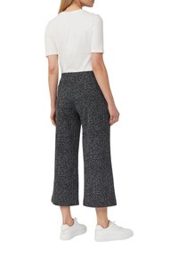 Haut blanc à manches courtes associé à un pantalon large à motifs noir et blanc, et des baskets blanches. La tenue présente une coupe décontractée.