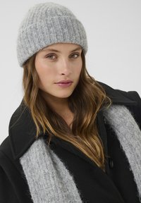 Grå strikket hue med ribbet tekstur, parret med en sort frakke og et bredt gråt tørklæde. Glatte materialer og neutral farvepalette.