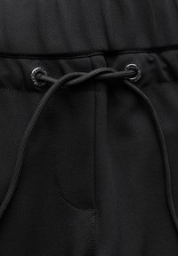 Zwarte sportieve broek van een getextureerde stof, met een elastische tailleband, een trekkoordsluiting met metalen hardware en zijzakken.