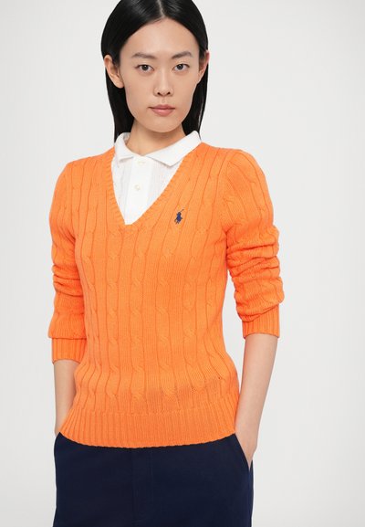 Oranžs adīts džemperis ar V-veida izgriezumu un ribotu apakšu, uz krūtīm ar mazu zilu logotipu un trīs ceturtdaļu piedurknēm.