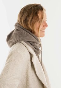 Gebreide sjaal met een geïntegreerde capuchon, in een zachte grijze kleur, met ribbeltextuur en trekkoorddetails, gedragen over een crèmekleurige jas.