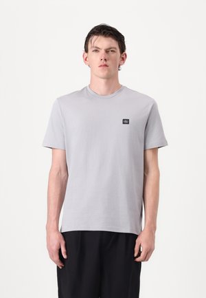 Grå bomulls t-shirt med rund halsringning och korta ärmar. Har en liten svart logotyp patch på bröstet och en avslappnad passform.