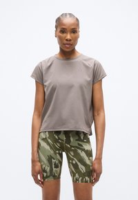 Αθλητική μπλούζα κοντομάνικη σε ανοιχτό γκρι με υφή στην επιφάνεια, συνδυασμένη με ποδηλατικά σορτς με πράσινο καμουφλάζ σχέδιο και ελαστική μέση.