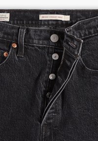 Pantalones vaqueros de mezclilla oscura con corte recto al tobillo, con cierre de botones, herrajes de cobre y plata, y un sutil desgaste en la tela.