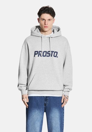 Szara bluza z kapturem z dużym granatowym logo "PROSTO." z przodu, z kieszenią typu kangur i ściągaczami przy rękawach. Noszona z niebieskimi dżinsami.
