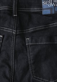 Jeans de mezclilla oscura con costuras claras en contraste, que cuentan con dos bolsillos traseros y una etiqueta en la cinturilla. Diseño estructurado y tela texturizada.