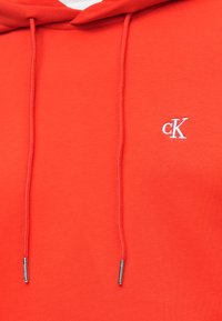 Piros kapucnis pulóver pamut keverékből, két húzózsinórral, elöl fehér hímzett "cK" logóval. Simább textúra, hétköznapi dizájn.