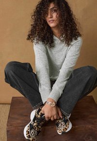 Grå sweater med ribbede manchetter, oversized mørke denim bukser og sorte sneakers med leopardmønster, kontrasteret af hvide såler.