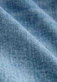 Gros plan sur un tissu en denim bleu clair montrant la texture du tissage diagonal et des plis subtils du tissu.