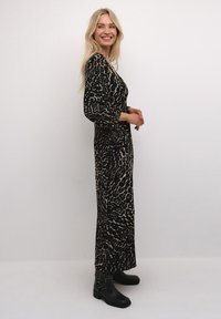 Pitkä musta mekko, jossa on vaaleanbeige eläinkuositi, tiukka siluetti ja kolmen neljänneksen hihat, yhdistettynä mustiin nilkkasaappaisiin.