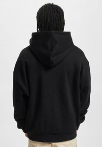 Sudadera negra con capucha amplia, corte oversize, puños y dobladillo acanalados. Textura suave con un diseño minimalista.