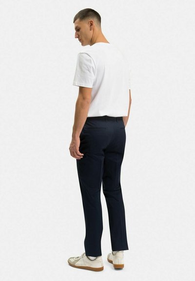 Vit bomull t-shirt, marinblå byxor och gräddvita sneakers. Byxorna har en smal passform med en jämn textur. Enkel och minimalistisk design.