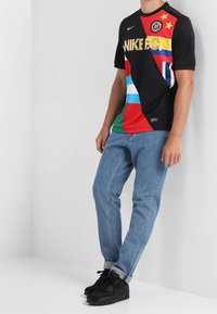 Černé tričko s krátkým rukávem s vícebarevnými panely a kulatým výstřihem. Na tričku je zlaté logo Nike. V kombinaci se světle modrými džíny a černými teniskami.