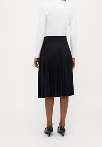 Svart veckad kjol med en bred midjeband, tillverkad av ett mjukt material. Kompletterad med svarta klackskor med en diskret klack.