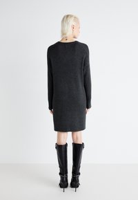 Robe pull tricotée de couleur gris foncé avec une coupe décontractée, des manches longues et une texture côtelée. Associée à de hautes bottes à talons noires.