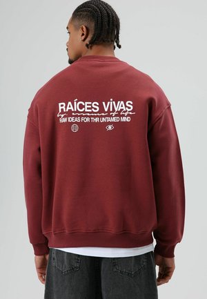 Bordeauxrode sweatshirts met tekst op de achterkant, voorzien van witte grafische afbeeldingen en een relaxte pasvorm. Geribbelde manchetten en zoom voegen textuur toe.