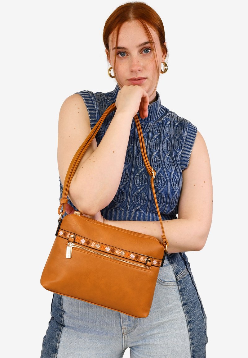 Bolso de cuero marrón claro con una correa ajustable, que cuenta con un bolsillo central con cremallera adornado con detalles florales y una textura suave.