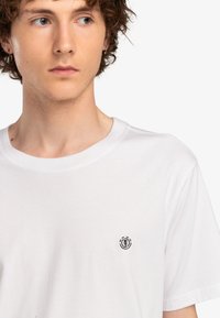 Hvid bomulds t-shirt med rund hals, med et lille sort logo på venstre brystområde. Blød tekstur og regular fit design.